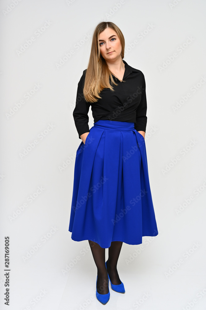 Full length vertical portrait of a cute brunette middle-aged manager woman with beautiful curly hair in a business suit and blue skirt on a white background. Beauty, brightness, smile. Full length vertical portrait of a cute brunette middle-aged manager woman with beautiful curly hair in a business suit and blue skirt on a white background. Beauty, brightness, smile.