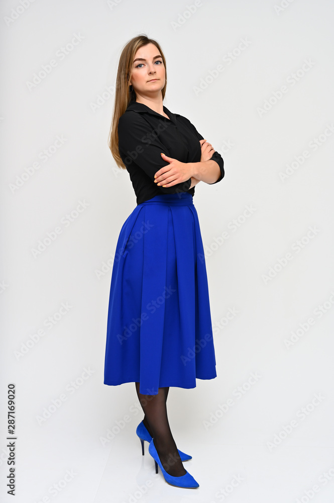 Full length vertical portrait of a cute brunette middle-aged manager woman with beautiful curly hair in a business suit and blue skirt on a white background. Beauty, brightness, smile. Full length vertical portrait of a cute brunette middle-aged manager woman with beautiful curly hair in a business suit and blue skirt on a white background. Beauty, brightness, smile.