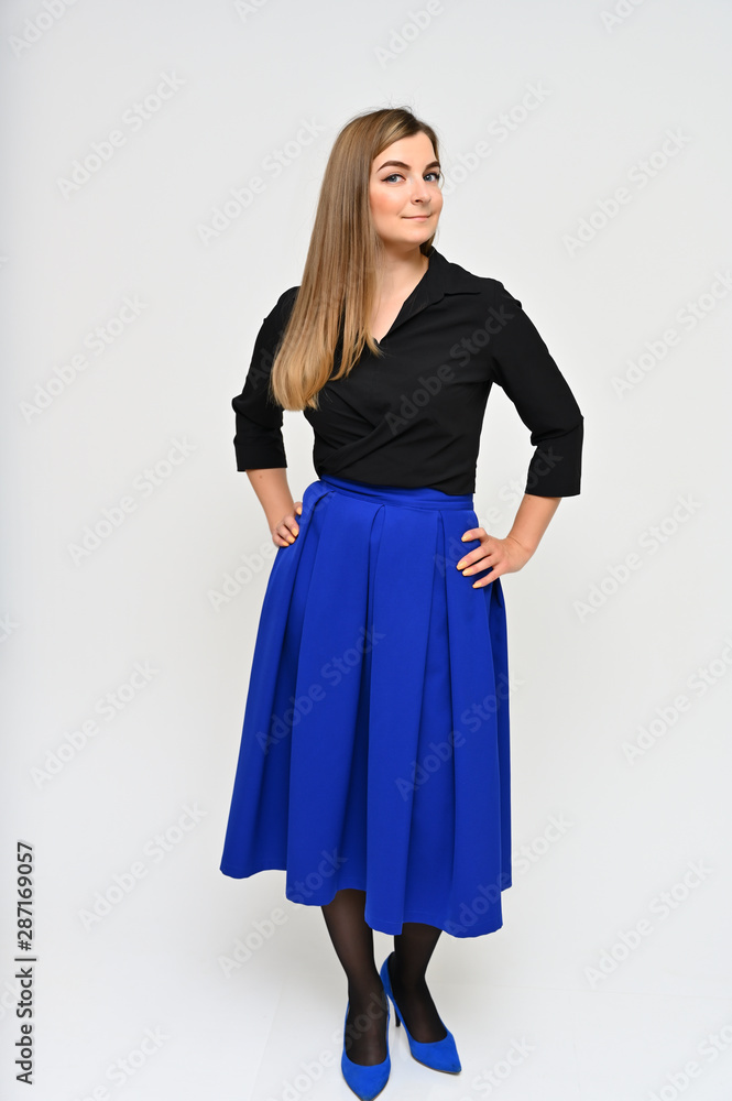 Fototapeta premium Full length vertical portrait of a cute brunette middle-aged manager woman with beautiful curly hair in a business suit and blue skirt on a white background. Beauty, brightness, smile.