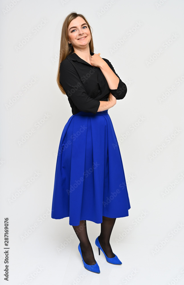 Fototapeta premium Full length vertical portrait of a cute brunette middle-aged manager woman with beautiful curly hair in a business suit and blue skirt on a white background. Beauty, brightness, smile.