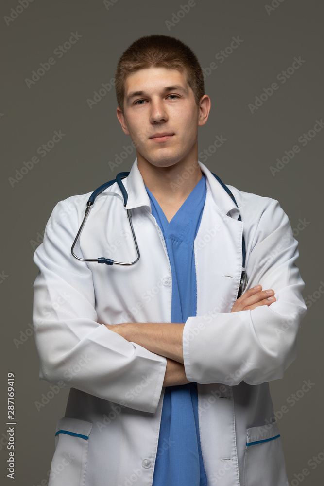 Portrait with copy space of cheerful joyful doctor in white lab coat and stethoscope on his neck, having his arms crossed, looking at camera, isolated on grey background. Portrait with copy space of cheerful joyful doctor in white lab coat and stethoscope on his neck, having his arms crossed, looking at camera, isolated on grey background.