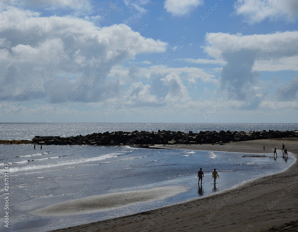 Sandy beach at low tide with people on the shore and blue sky with clouds, La Laja, coast of Las Palmas de Gran Canaria 
