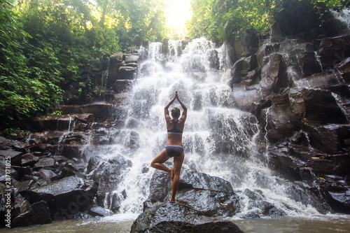 Woman practices yoga near waterfall in Bali  Indonesia