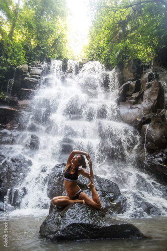 Woman practices yoga near waterfall in Bali, Indonesia