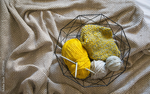 Basket with yarn and knitting neddles on cozy blanket, top view photo