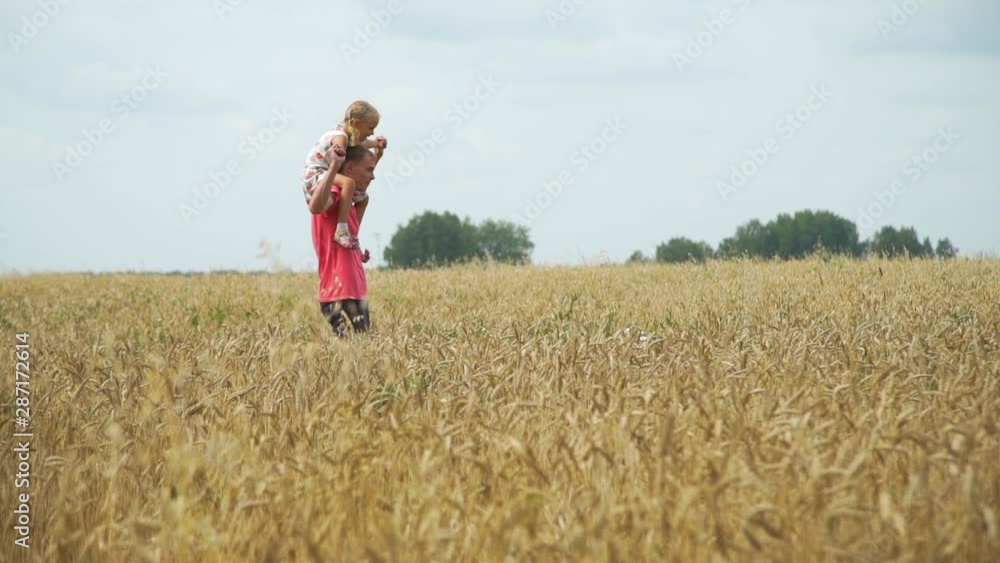 Adult Man Carrying his Little Daughter on Neck while Walking Through the Golden Wheat Field. They are Moving from Left Side of a Screen to Right. Adult Man Carrying his Little Daughter on Neck while Walking Through the Golden Wheat Field. They are Moving from Left Side of a Screen to Right.