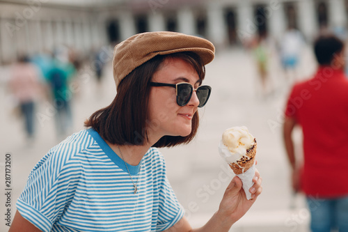 Young smiling  woman with cone gelato ice cream in hand in striped frock vest   white pants and cap at  Piazza San Marco place  Venice  Veneto  Italy