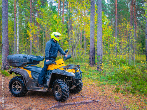 Riding an ATV. ATV man side view. ATV adventure. A man on an quadrocycle examines the surroundings. Trips through the autumn forest. Young man on a yellow quadrocycle.Human rides an quad bike. Leisure