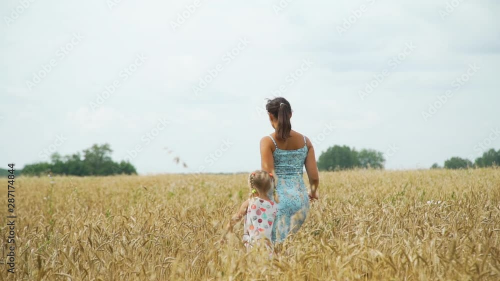 Young Woman with her Cute Little Daughter Walking in the Wheat Field. Back Side View. Slow Motion. Freedom and Enjoying Nature Concept Young Woman with her Cute Little Daughter Walking in the Wheat Field. Back Side View. Slow Motion. Freedom and Enjoying Nature Concept