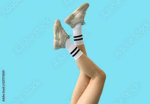 Stylish young woman in shoes and socks on color background