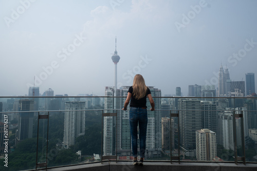 Back view of woman on the top floor of a skyscraper admires the view of Kuala Lumpur, Malaysia photo