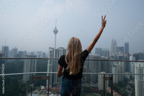 Back view of woman on the top floor of a skyscraper admires the view of Kuala Lumpur  Malaysia