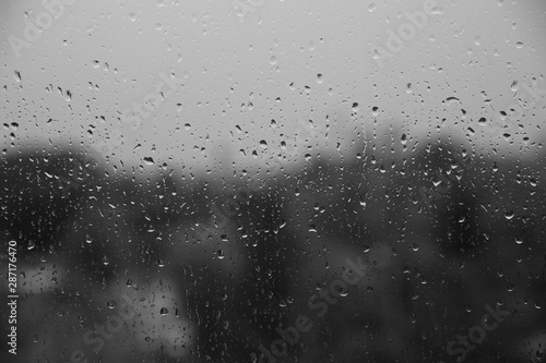 rain drops on window close up, behind gray blurry view, monochrome black and white