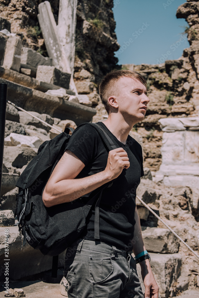 Tour of the ancient cities of Turkey.Man at the amphitheater in Side.Young man with big black backpack. Traveler. Holidays in Turkey. Stylish young man