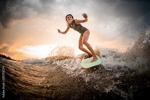Skinny girl riding on the wakeboard on the river on the wave on the bending knees