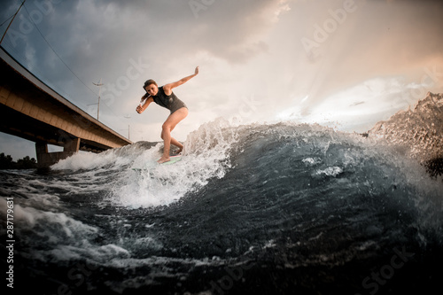 Girl riding on the wakeboard on the river in the background of the bridge rising hands up