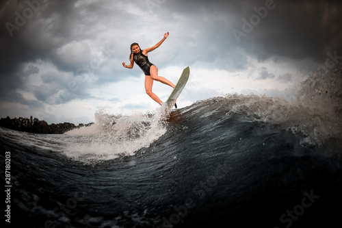 Sporty girl jumping on the wakeboard on the river in the background of trees rising hands