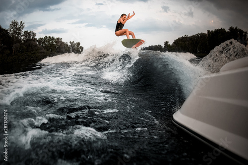 Girl jumping on the wakeboard on the river on the wave of the motorboat