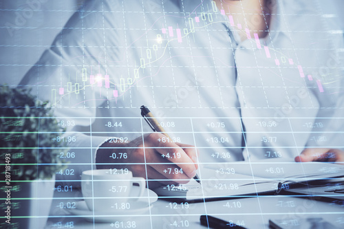 Double exposure of man's hands writing notes of stock market with forex chart.