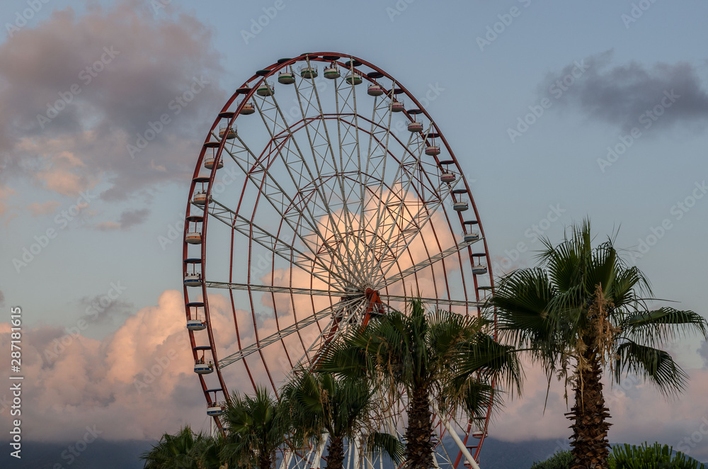 Batumi,Adjara,Georgia - July 06 2019, Batumi embankment, Ferris wheel in the rays of the setting sun, unusually colored clouds,