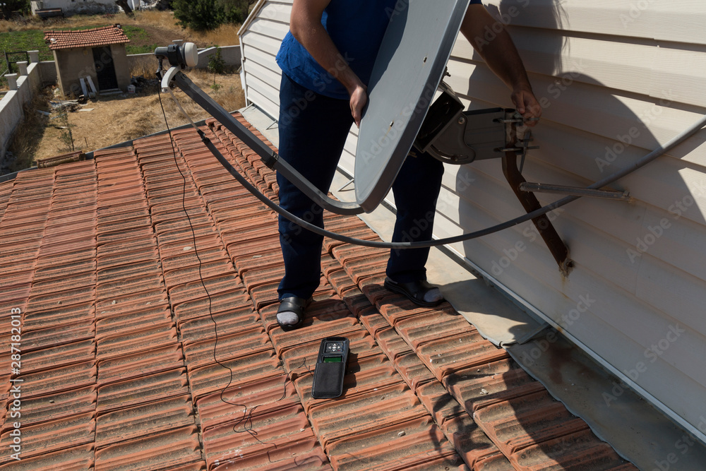 the worker repair the antenna at the house roof with satellite device.