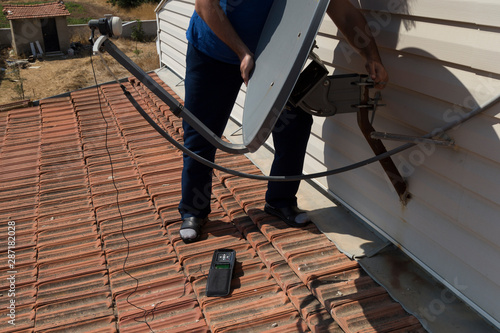 the worker repair the antenna at the house roof with satellite device.