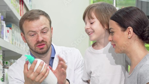 Cheerful male pharmacist helping young woman with little son. Female customer shopping at drugstore with her child, asking chemist for an advice. Service, healthcare concept