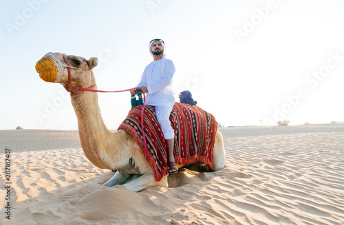 Arabian man with traditional clothes riding his camel photo