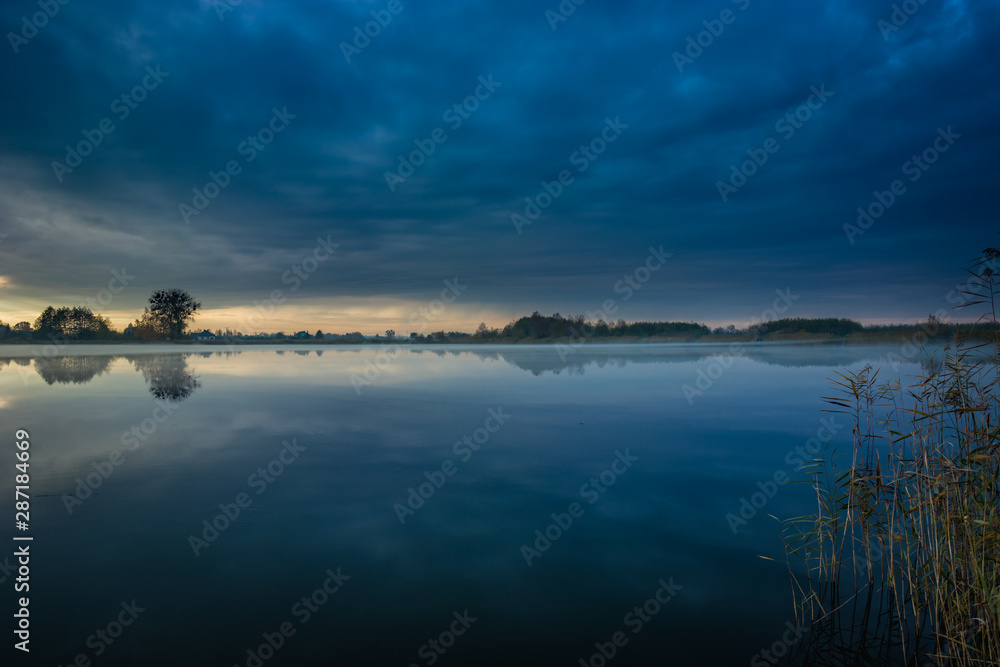 Dark blue clouds over the lake with fog and reeds