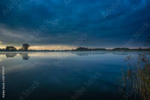 Dark blue clouds over the lake with fog and reeds