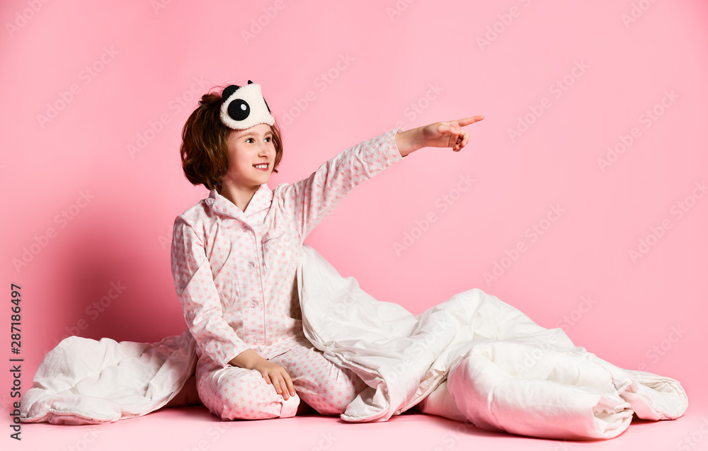 gorgeous smiling girl wearing eye mask carrying a pillow and blanket. Isolated on pink pastel background. - obrazy, fototapety, plakaty 