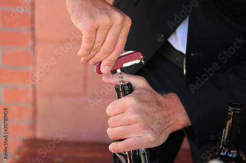 Corkscrew in the hands of a sommelier who opens a bottle of wine. Photo without a face. Hands close up. Wine tasting concept.