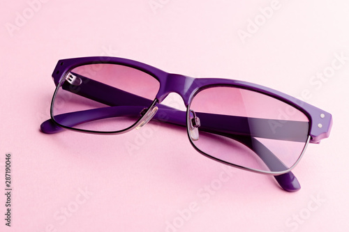 Fashionable purple color sunglasses closeup on pink background