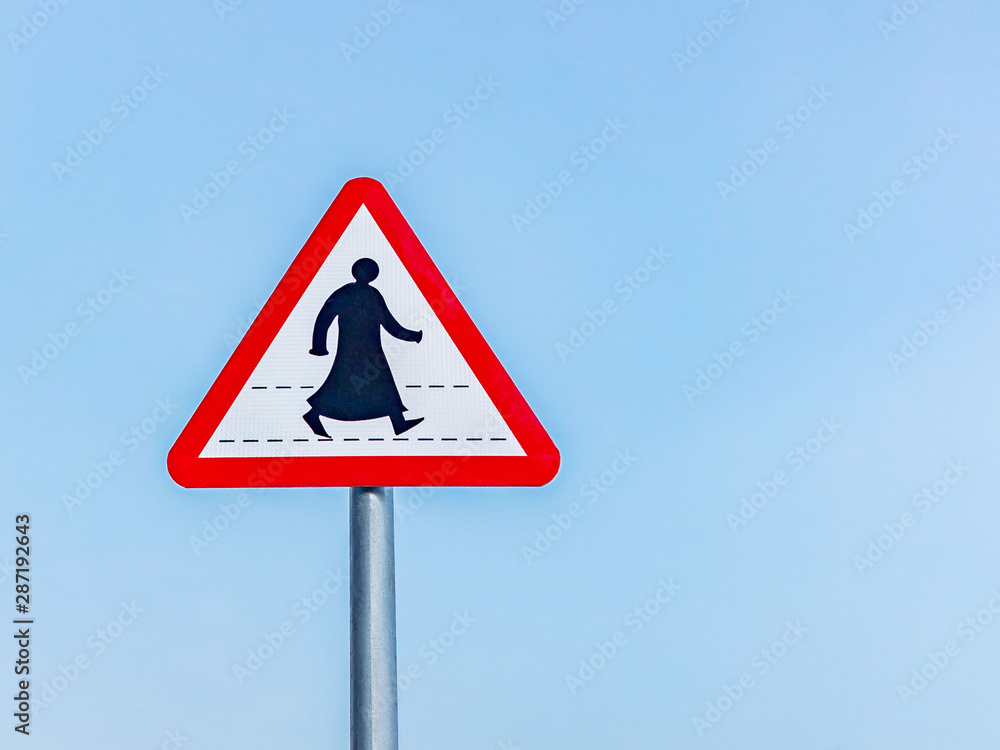 Sign prohibiting traffic for pedestrians in a southern Arab country, a silhouette of a pedestrian in traditional clothes, against a blue sky Sign prohibiting traffic for pedestrians in a southern Arab country, a silhouette of a pedestrian in traditional clothes, against a blue sky