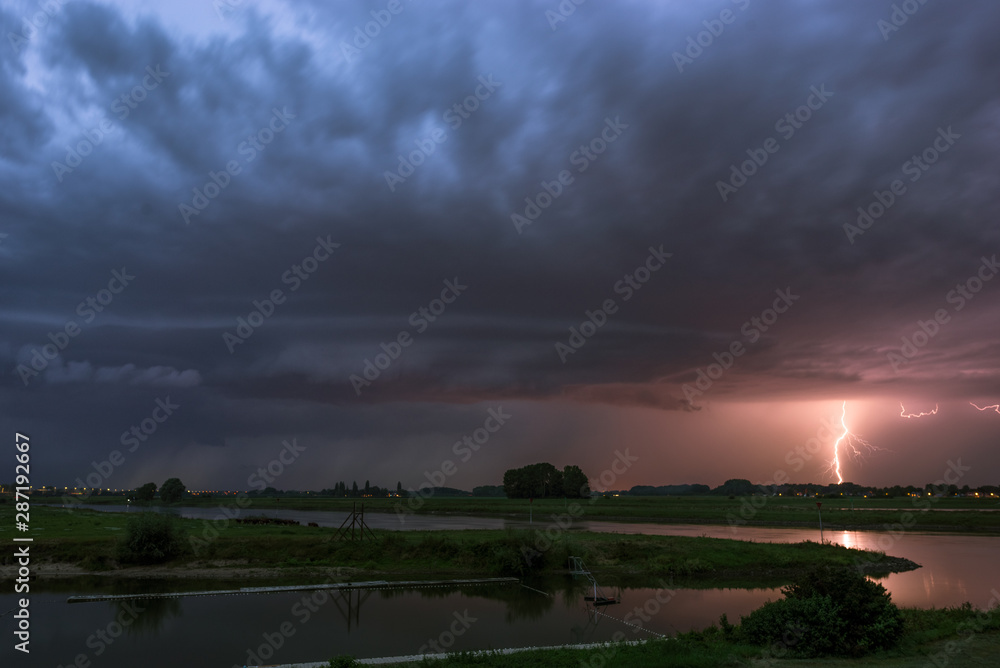 Shelfcloud and lightning from a severe thunderstorm near a river at dusk Shelfcloud and lightning from a severe thunderstorm near a river at dusk