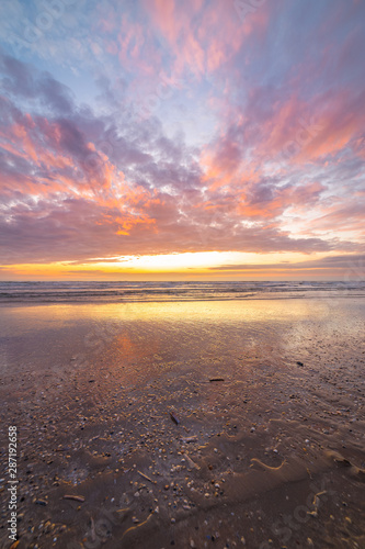 Vertical view of a colorful sunset at the beach. Beautiful reflections of the evening sky in the wet sand.