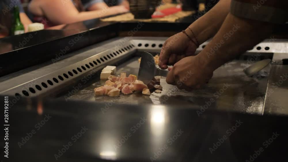 Asian chef slising chicken meat for the audience on a large stove