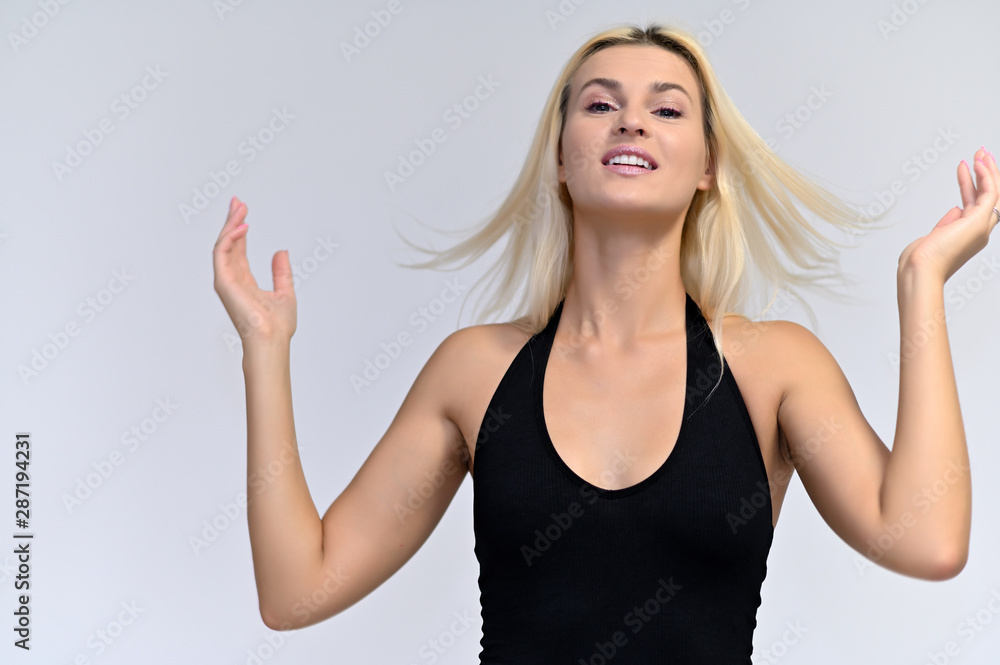 Fototapeta premium Portrait of a cute girl, a young blonde woman with beautiful curly hair in a black T-shirt on a white background. Beauty, brightness, smile, emotions.