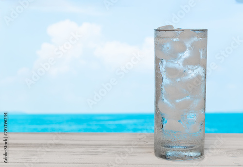 Refreshment glass of drink water with ice on white wood table with summer sea sky background.