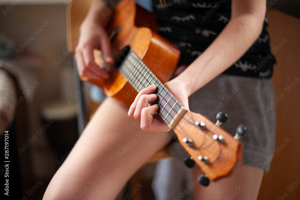 Fototapeta premium The girl plays on the ukulele. Playing guitar. Music lessons. A girl creates a melody of a song on a musical instrument.