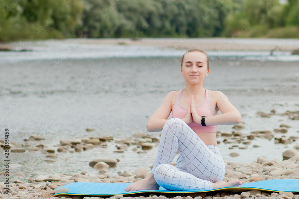 healthy girl relaxing while meditating and doing yoga exercise in the beautiful nature on the bank of the river