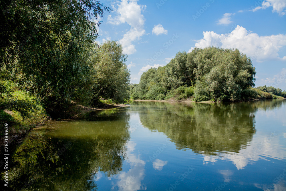 Blue beautiful sky against the background of the river. Clouds are displayed in calm water. On the horizon, the green bank of the Dniester, place for fishing