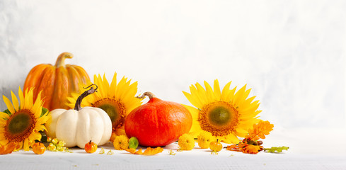 Beautiful autumn still life with sunflowers, red- yellow flowers, autumn leaves and white and orange pumpkins on wooden table, front view. Autumn concept with pumpkins and flowers.