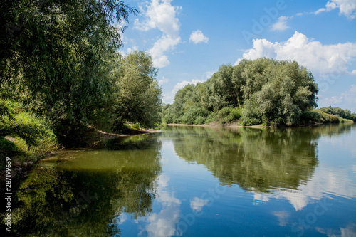 Blue beautiful sky against the background of the river. Clouds are displayed in calm water. On the horizon, the green bank of the Dniester, place for fishing © volody10