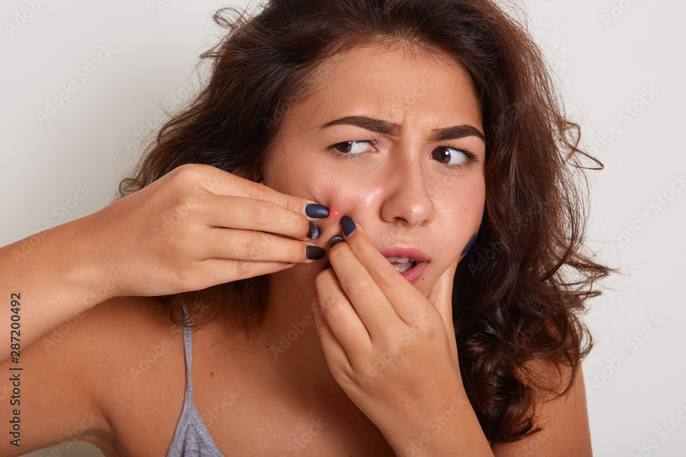 Young girl anxiously looking in mirror, holding her hands near her face, posing isolated over white background, lady looking away, having problems with skin, has acneonher face, dressed gray t shirt Young girl anxiously looking in mirror, holding her hands near her face, posing isolated over white background, lady looking away, having problems with skin, has acneonher face, dressed gray t shirt