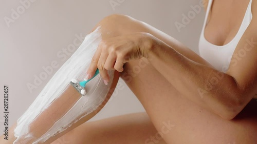 Shaving legs. Close up side view of a young woman shaving her legs