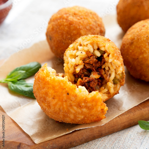 Homemade fried Arancini with basil on a rustic wooden board, side view. Italian rice balls. Close-up. photo