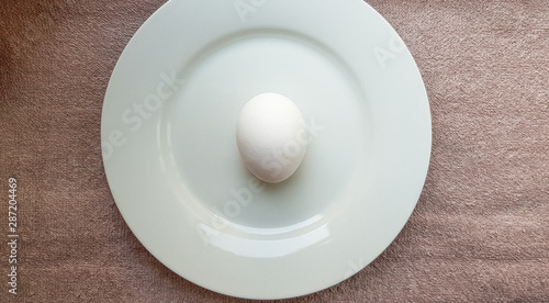 One whole raw chicken white egg on a white plate