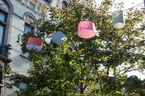 Lamp shades are hung on a wire and used as street lighting.Trees and building as backdrop in this street scene. Aarschot Belgium - Image photo