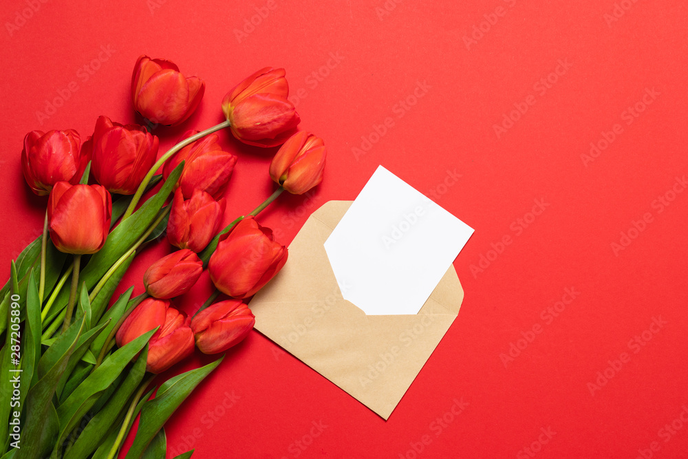 Envelopes with space for text and beautiful red tulips on a red background. Close Envelopes with space for text and beautiful red tulips on a red background. Close